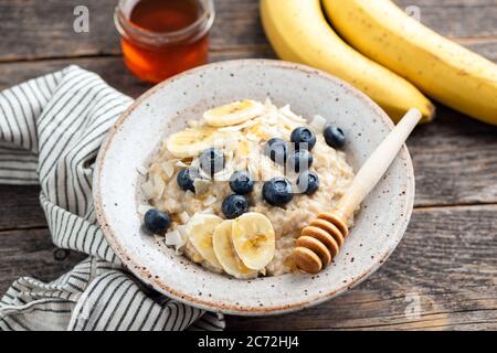 Porridge de flocons d'avoine avec bleuets, bananes et miel dans un bol sur table en bois. Concept de nourriture saine pour le petit déjeuner Banque D'Images