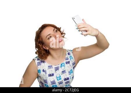 Portrait d'une jeune fille en surpoids à tête rouge sur un fond blanc isolé, photographié en profil, se berner et prendre un selfie Banque D'Images