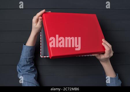 Les mains des enfants ouvrent une boîte cadeau avec un couvercle rouge. Vue de dessus. Banque D'Images