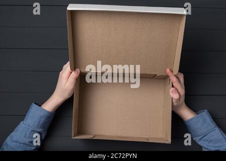 Mains des enfants tenant une boîte en carton ouverte. Boîte vide, fond noir. Banque D'Images