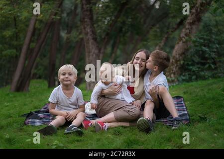 Bonne famille de quatre personnes ayant pique-nique à la prairie. Mère et trois enfants assis sur une couverture de pique-nique. Banque D'Images
