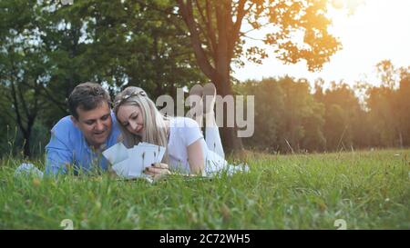 Un gars et une fille regardent un album de famille avec des photos dans le parc sur l'herbe. Banque D'Images