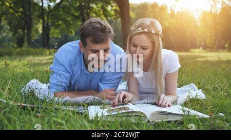 Un gars et une fille regardent un album de famille avec des photos dans le parc sur l'herbe. Banque D'Images