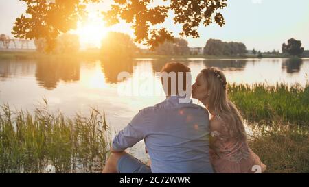 Un jeune couple est assis sur un lac au coucher du soleil. Banque D'Images