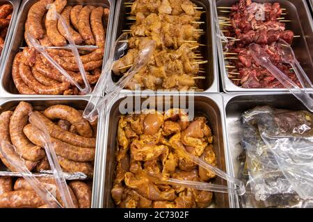 Divers produits de viande fraîche sur le réfrigérateur de présentation de boucher dans le restaurant de bistro. Saucisses, brochettes de volaille et de rouge, viandes assaisonnées prêtes à cuire. Banque D'Images