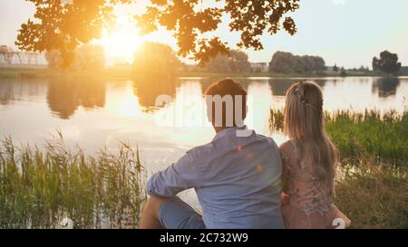 Un jeune couple est assis sur un lac au coucher du soleil. Banque D'Images