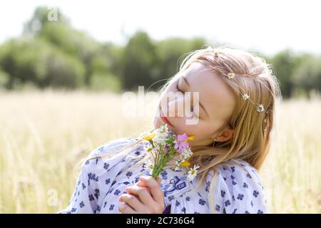 Une jeune fille assez hippie avec des cheveux blonds tient une posy de fleurs sauvages au soleil dans un champ de pâturage en été. Banque D'Images