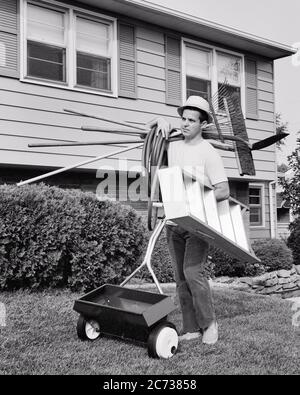 HOMME DES ANNÉES 1970 PROPRIÉTAIRE À CHAPEAU JEANS BASKETS MARCHE DANS COUR AVANT POUSSER L'ÉPANDEUSE DE PELOUSE TENANT L'ÉCHELLE FLEXIBLE RÂTEAU PELLE ET BALAI - G8019 HAR001 HARS VIE VIE VIE COPIE ESPACE PLEINE LONGUEUR PERSONNES BALAI RÉSIDENTIEL MÂLES BÂTIMENTS BASKETS CONFIANCE B&W JARDINIER COMPÉTENCES PROFESSIONNELLES ET EXTÉRIEUR DANS LES MAISONS PROFESSIONS SEMENCES ENTRETIEN COUR TRAVAIL CONCEPTUEL PROPRIÉTAIRE MAISON SOUTIEN MAISON DIY AMÉLIORATION MAISON ADULTE MOYEN-ADULTE HOMME TÂCHE NOIR ET BLANC CAUCASIEN ETHNICITÉ HANDYMAN HAR001 PROPRIÉTAIRE MAISON ANCIEN MODE Banque D'Images