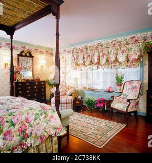 CHAMBRE DES ANNÉES 1990 INTÉRIEUR CHINTZ FLORAL SUR LE PAPIER PEINT DE LA COUVERTURE DE LIT ET RIDEAUX LIT À BALDAQUIN BUREAU MIROIR - KI10150 TEU001 MOBILIER HARS ANCIEN STYLE Banque D'Images