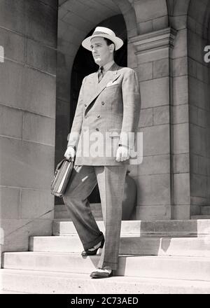 HOMME DES ANNÉES 1940 MARCHANT SUR DES MARCHES TENANT UNE MALLETTE PORTANT UN GLEN PLAID DOUBLE COSTUME CROISÉ SPECTATEUR CHAUSSURES WINGTIP POIDS D'ÉTÉ CHAPEAU - S9479 HAR001 HARS PLAID CONFIDENCE B&W COSTUME ET CRAVATE VÊTEMENTS DE VENTE EXTÉRIEUR BAS ANGLE GLEN OCCUPATIONS SPECTATEUR ÉLÉGANT VÊTEMENTS DE SPORT DE SAISON DE BRASSIÈRE VENDEURS JEUNES ADULTES NOIR ET BLANC RACE BLANCHE HAR001 DÉMODÉE Banque D'Images