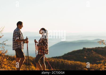 Jeune femme enceinte avec petit ami nordic marchant en plein air avec des bâtons de randonnée. Un mode de vie actif et sain en maternité. Belle vue sur la montagne en automne. Banque D'Images