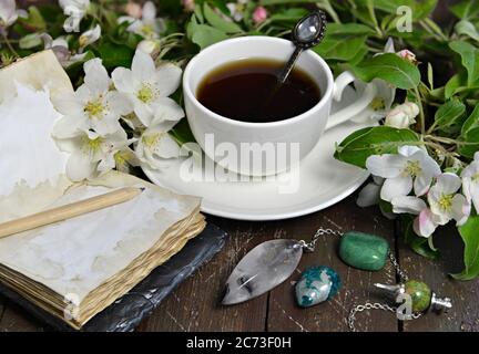 Tasse de thé avec journal ouvert et fleurs de pommier sur planches. Arrière-plan ésotérique, gothique et occulte avec objets magiques, concept mystique et conte de fées Banque D'Images