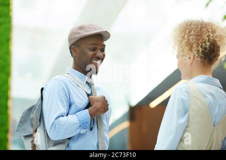 Joyeux homme africain parlant à la jeune femme et souriant pendant leur réunion à l'extérieur Banque D'Images