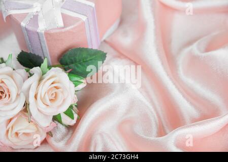 Bouquet de roses roses et boîte cadeau avec noeud sur fond de tissu en soie rose ondulé. Vide pour la carte de vœux avec espace de copie Banque D'Images