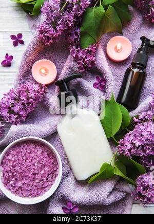 Cadre spa avec fleurs de lilas. Sel de mer dans un bol, bouteilles d'huile aromatique et bougies sur fond de bois. Banque D'Images