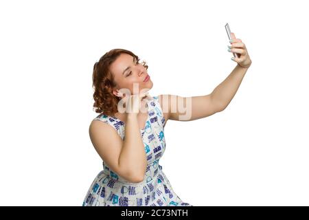 Portrait d'une jeune fille en surpoids à tête rouge sur un fond blanc isolé, photographié en profil, se berner et prendre un selfie Banque D'Images