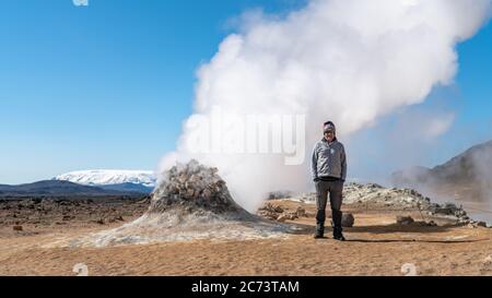 Hverir, Islande - Mai 2019: Touriste debout à côté d'un évent de vapeur dans la zone géothermique de Hverir Myvatn, explorant les évents à vapeur naturels et les piscines de boue tous ar Banque D'Images