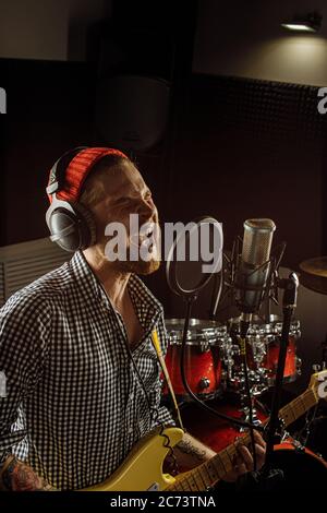 un musicien de race blanche joue de la guitare électrique et chante en studio d'enregistrement. homme se préparant, s'exerçant avant la performance musicale, avant le concert. musi Banque D'Images