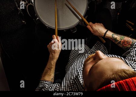 jeune batteur caucasien qui répète sur des tambours avant un concert de rock. artiste professionnel qui enregistre de la musique sur un tambour dans un studio sombre Banque D'Images