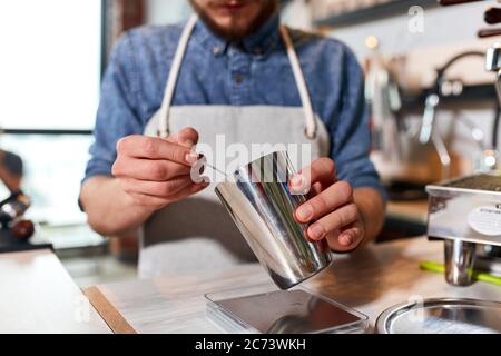 Les mains du barista prennent un peu de café moulu dans une verseuse métallique avec une petite cuillère, retirent le café supplémentaire de la cuve, concept de service Banque D'Images