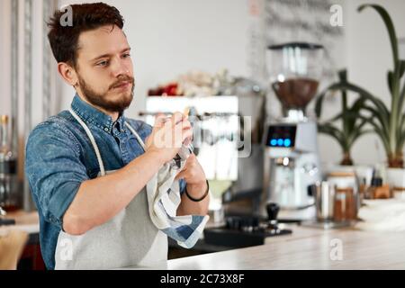 Un barista masculin compétent et compétent, avec une barbe épaisse et élégante, des drys avec une vadrouille, un regard bien pensé, se tient au comptoir du bar, un concept de nettoyage, un portrait Banque D'Images