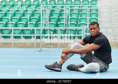 Athlète pensif sérieux regardant en étant assis sur la route après les classes de PE. Photo pleine longueur. Espace de copie Banque D'Images