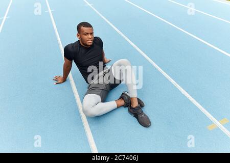 coureur afro fatigué en sueur assis sur la route, photo pleine longueur. espace de copie. temps libre, temps libre, style de vie Banque D'Images