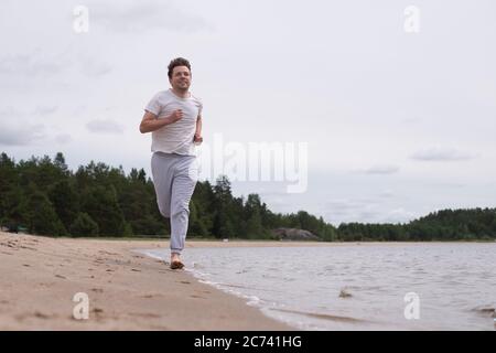 Homme dans des vêtements de fitness courant le long de la plage de sable Banque D'Images