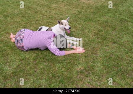 Femme caucasienne mature et jeune chien blanc mixte allongé sur une pelouse coupée en été Banque D'Images