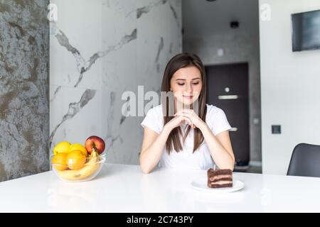 Concept de régime. Alimentation saine. Belle jeune femme qui choisit entre fruits et sucreries Banque D'Images