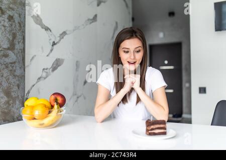 Concept de régime. Alimentation saine. Belle jeune femme qui choisit entre fruits et sucreries Banque D'Images