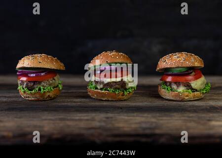 Hamburgers aux tomates, oignons, concombre, laitue et fromage fondu servis sur une table rustique en bois Banque D'Images