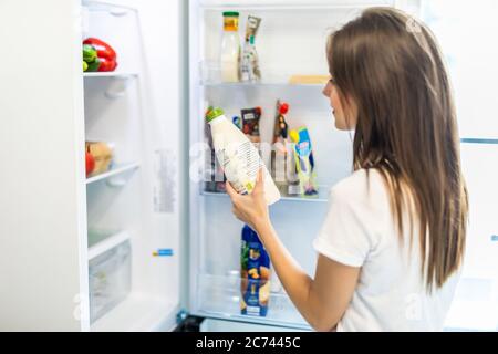 Une femme a choisi du lait dans un réfrigérateur ouvert, un réfrigérateur frais et neuf rempli de nourriture biologique savoureuse, une femme se préparant à cuisiner, concept de saine alimentation Banque D'Images