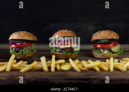 Hamburgers aux tomates, oignons, concombre, laitue, fromage fondu et frites servis sur une table rustique en bois Banque D'Images