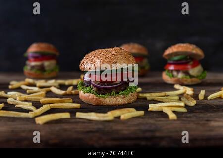 Hamburgers aux tomates, oignons, concombre, laitue, fromage fondu et frites servis sur une table rustique en bois Banque D'Images