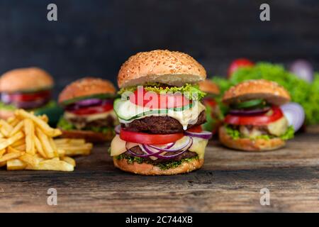 Double hamburger avec tomates, oignons, concombre, laitue, fromage fondu et frites servis sur une table rustique en bois Banque D'Images