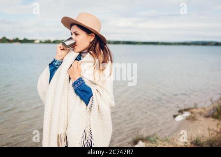 Femme voyageur dans le chapeau aime la vue sur le lac paysage boire le thé chaud couvert avec une couverture. Concept de voyage et de tourisme Banque D'Images