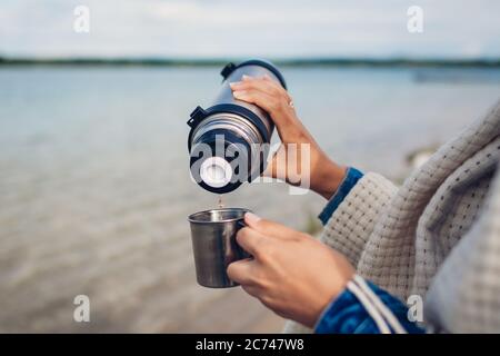 Le thé chaud au chaud au bord du lac d'automne. Camping, voyager. Gros plan des mains avec la cuvette Banque D'Images