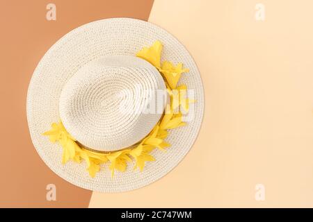 Chapeau de paille avec fleurs de nénuphars jaunes sur fond pastel et terre cuite. Modèle rétro élégant. Fond jaune. Concept de mode d'été. Banque D'Images