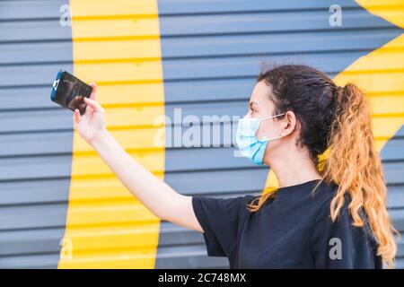 Adolescent faisant un selfie dans la rue portant un masque. Jeune femme protégée par un masque. Selfie avec masque. La vie humaine à distance sociale. Sécurité et pa Banque D'Images