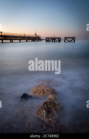 Lever du soleil à la mer avec de l'eau en mouvement sur des rochers et un quai entouré par l'eau calme Eastney, Southsea UK Banque D'Images