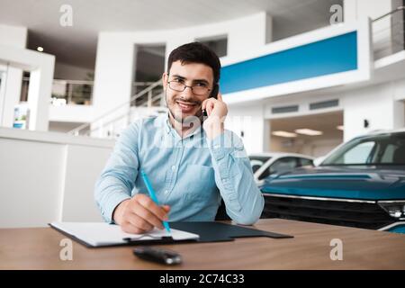 Employé de l'établissement concessionnaire automobile qui parle au téléphone et écrit Banque D'Images