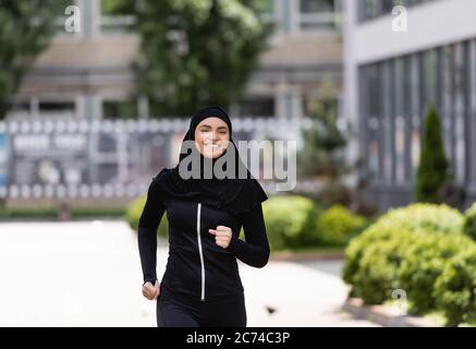 fille arabe souriante dans le hijab et sportswear jogging à l'extérieur Banque D'Images