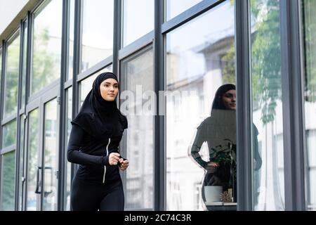 femme arabe dans hijab et sportswear jogging près du bâtiment Banque D'Images