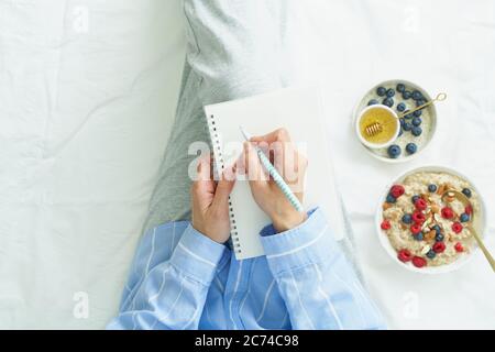 femme écrit dans un grand carnet blanc ouvert, couché sur le lit Banque D'Images