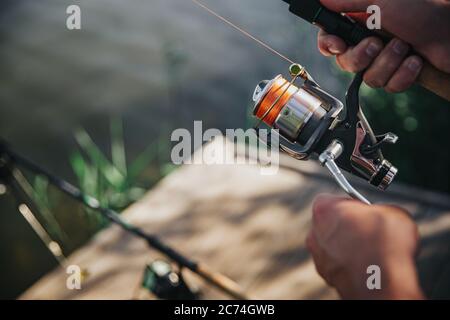 Jeunes pêcheurs pêchant sur le lac ou la rivière. Couper la vue et le gros plan des mains de l'homme tirant et de la bobine en les utilisant pour attraper un peu de poisson. Tenez-vous à proximité de Banque D'Images