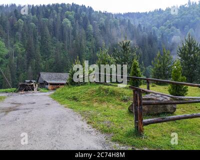 Route le long de la clôture rustique en rondins qui s'invente dans une cabane et une pile de bois au milieu de la forêt à feuilles persistantes au fond des montagnes carpates. Retraite tranquille et isolée. Banque D'Images