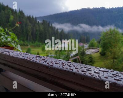 Vue depuis le balcon ouvert sur les nuages bas, forêt sauvage, montagne de Trostyan Carpates, sièges de télésiège et bâtiment de station. Balcon avec gouttes de pluie. Banque D'Images