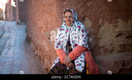 Abyaneh, Iran - Mai 2019 : une vieille femme aux vêtements traditionnels persans est assise dans une vieille rue d'Abyahen, un site iranien de l'UNESCO Banque D'Images