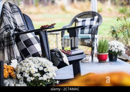 Fauteuil à bascule Adirondack avec couverture à carreaux de style traditionnel et oreillers sur une véranda ou un patio décoré pour l'automne avec des gourdes et des wh Banque D'Images